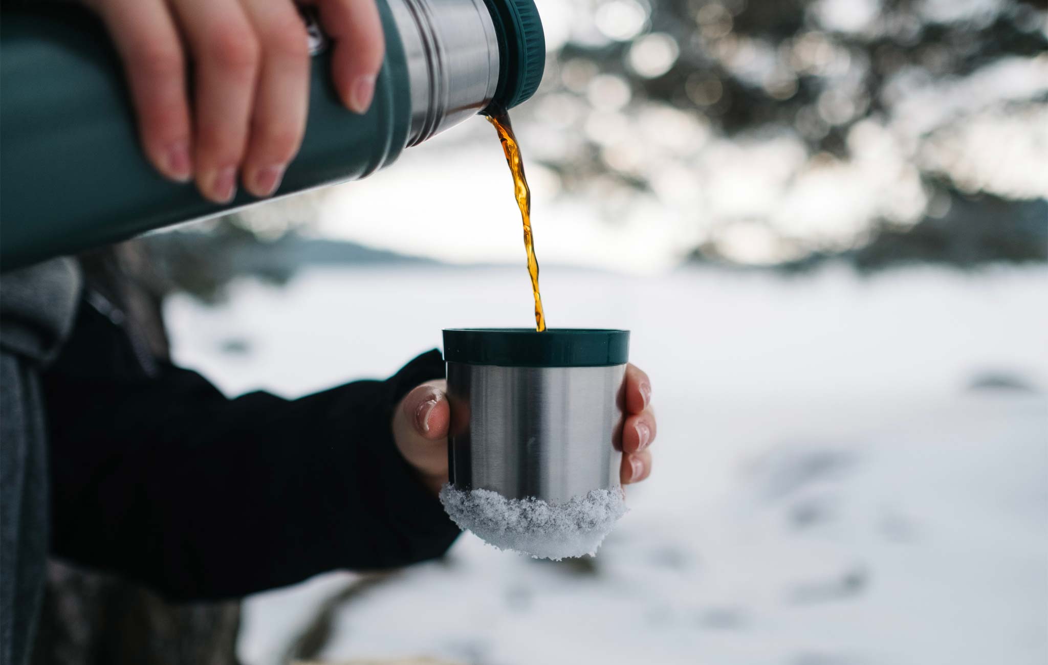 person pouring coffee out of a thermos in winter