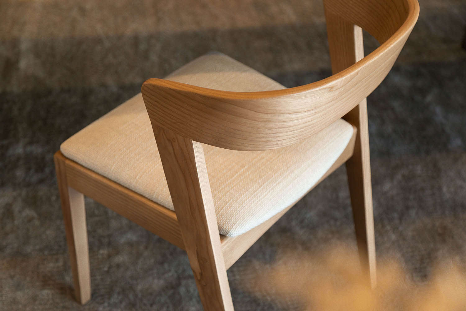 Woodbender Vuti dining chair close up, showing detail of wood and upholstery. Woodbender dining chairs and bar stools are available via Sarza furniture store in Rye, New York