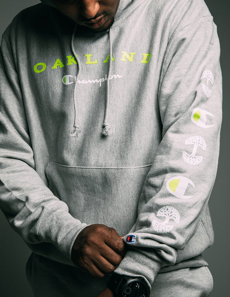 On grey fleece, highlighter green and white, OAKLAND and Champion logo, front print and sleeve print.