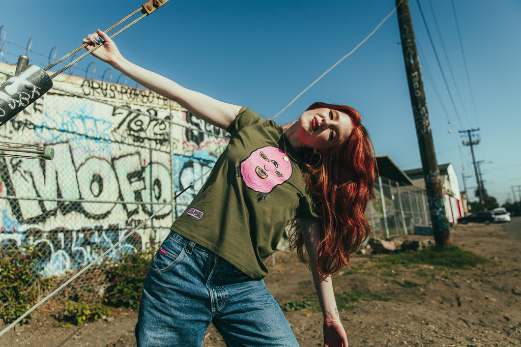 Girl model with red hair wearing green tee with illustration of girl in a pink ski mask.