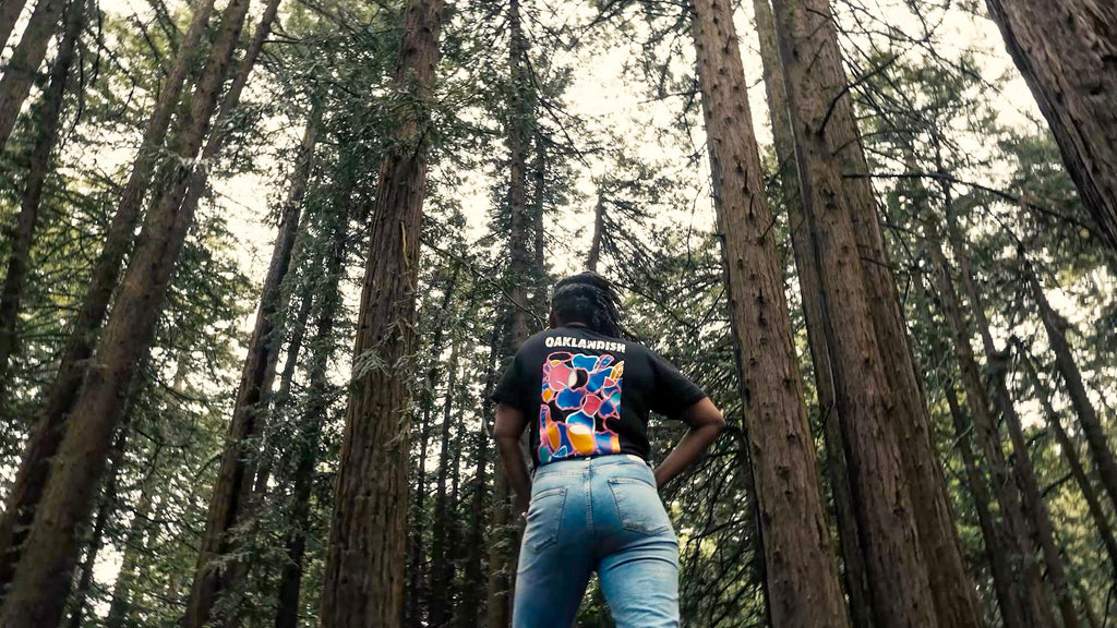 Female model in the woods, we see her back with large multicolor print.