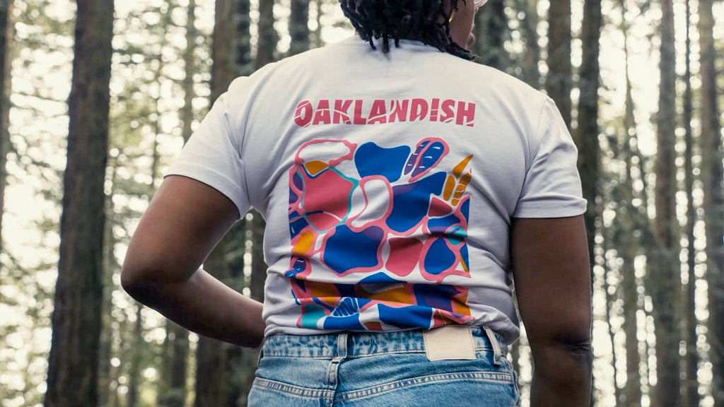 DJ Red Corvette wearing white tee with multicolor back print, in the woods.