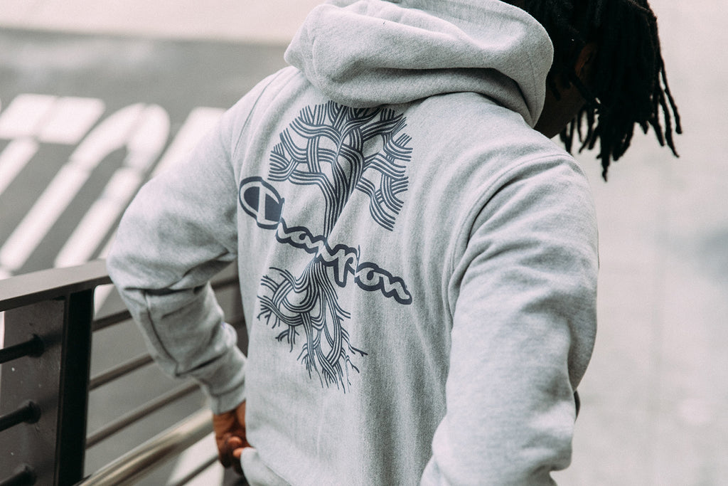 Back of grey hoodie with dark grey ink showing Oaklandish tree with Champion wordmark logo through the center of the tree.