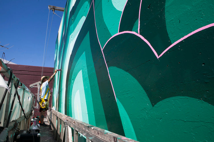 artist on scaffolding, painting on wall in green paints