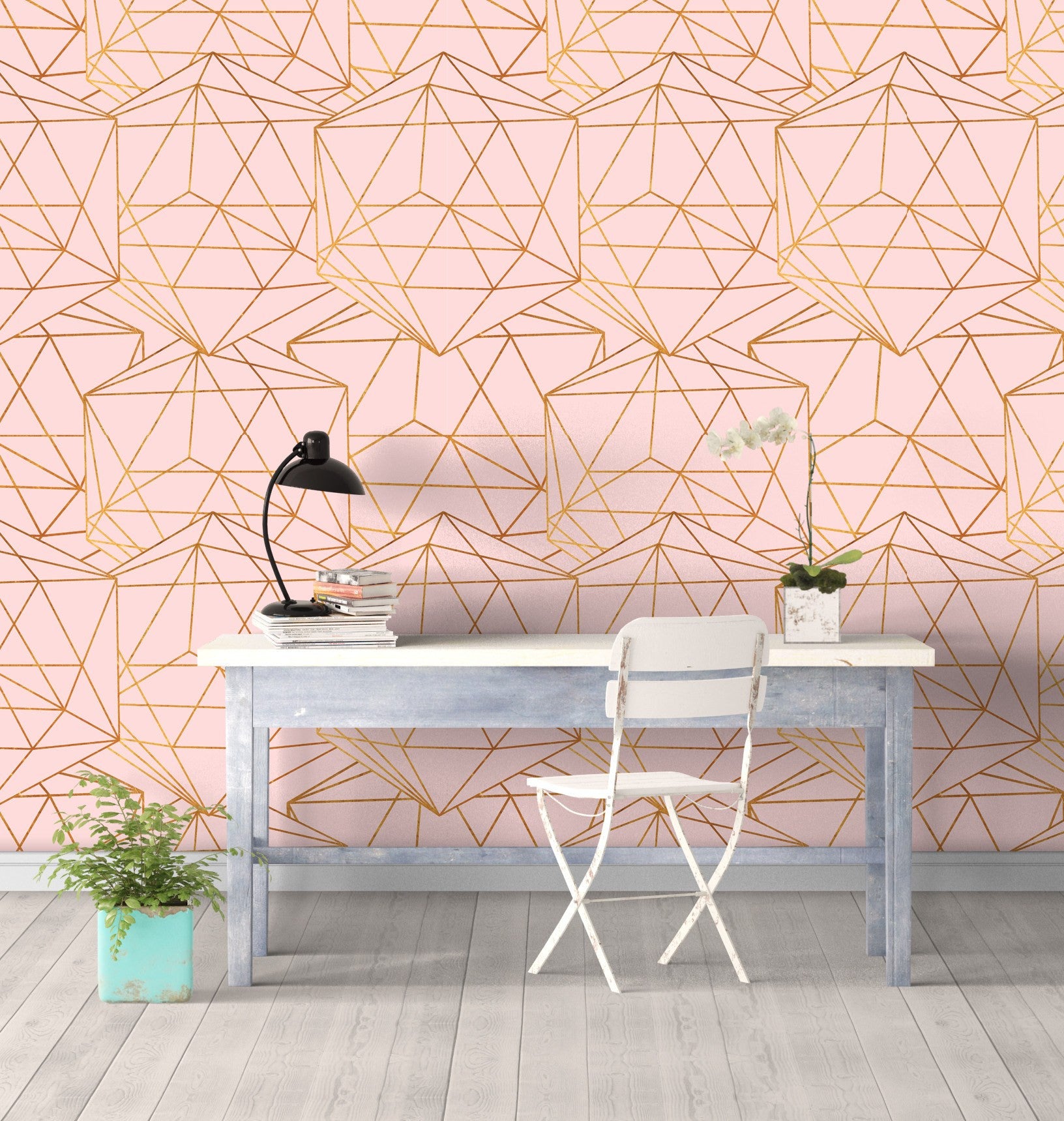 A small desk with a white chair sits up against a wall covered in pink wallpaper with an all-over gold geometric pattern.