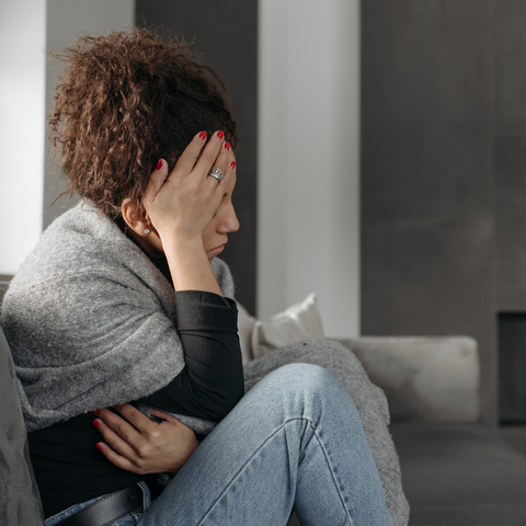A woman sat down on a sofa holding her head, experiencing a headache.