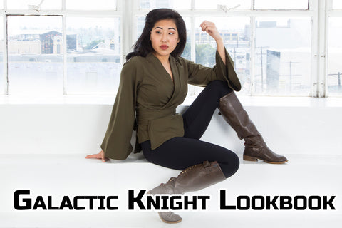 Galactic Knight Collection  - Kate (a medium skinned model with dark hair) wears an olive green wrap top, leggings, and boots while sitting on steps in front of a windowed wall. The wrap top is part of our Galactic Knight Collection, inspired by space kni