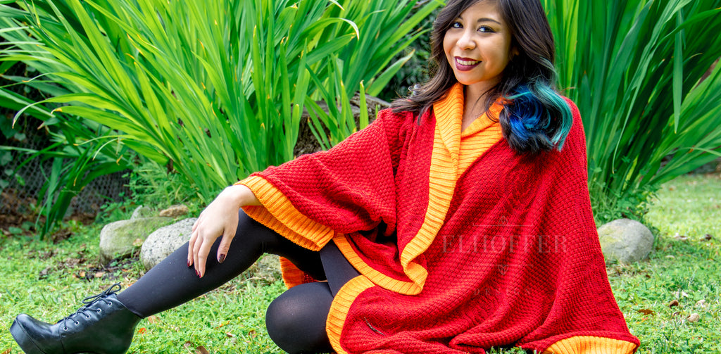 Melanie, a medium light skinned model with dark hair, models the Galactic Appeal Dolman. The dolman is a bright red textured knit with orange cuffs and hems.