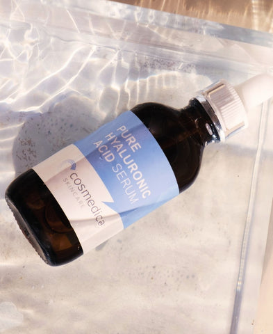 A bottle of Cosmedica Skincare Pure Hyaluronic Acid Serum lying in water. 