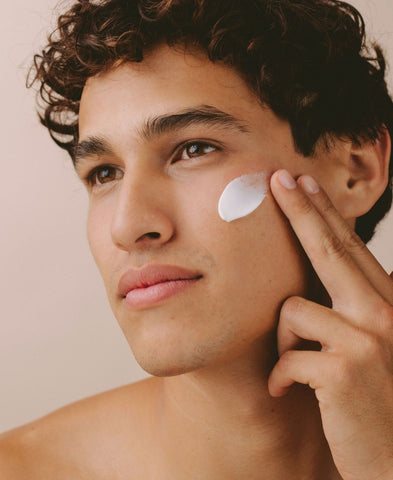 Close up of a young man applying moisturizer to his face. 