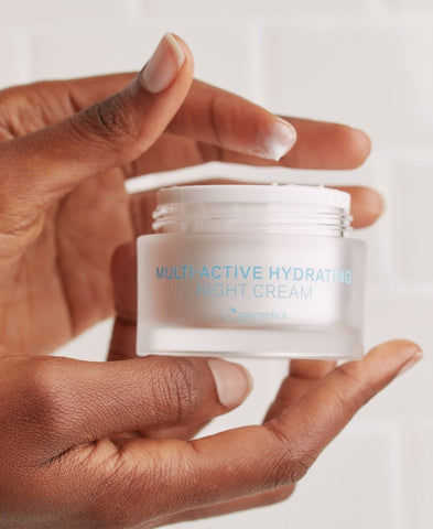 A pair of hands holding an open jar of Cosmedica Skincare's Multi-Active Hydrating Night Cream. 