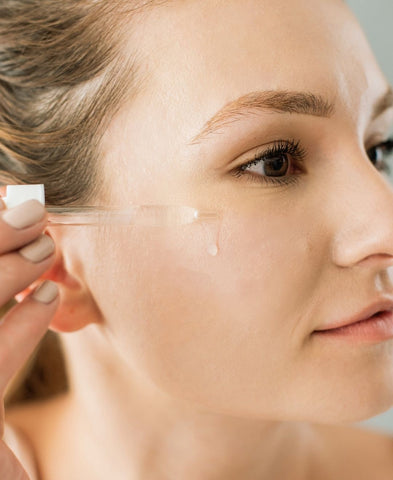 Close up of woman applying hyaluronic acid serum to her face. 