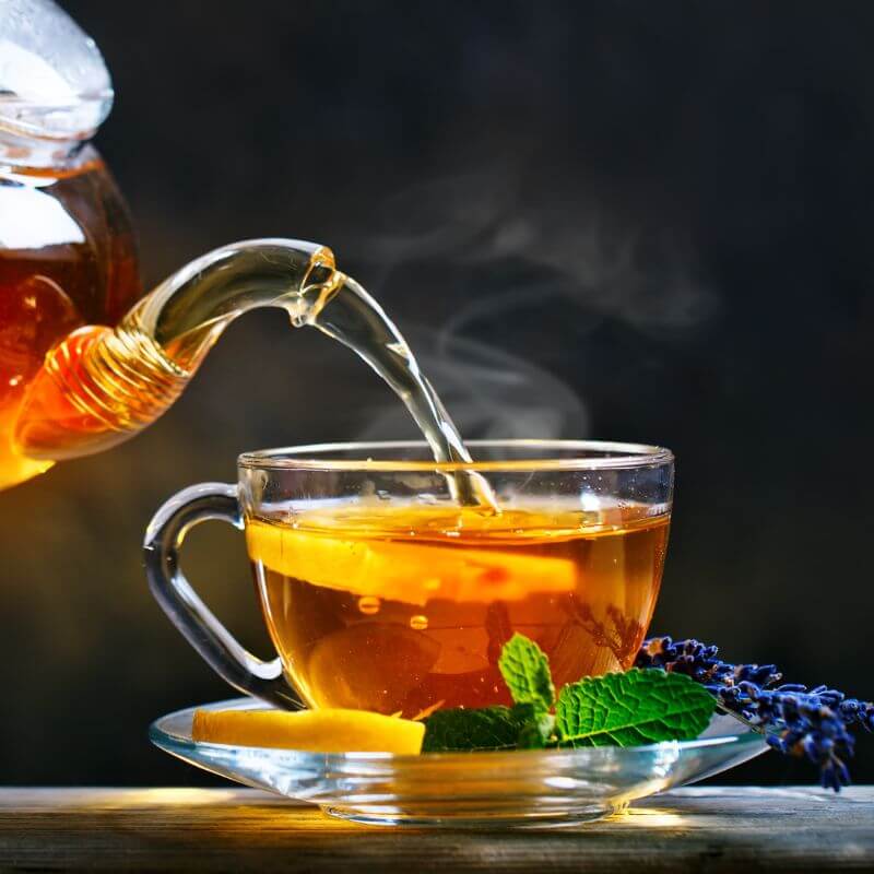 Perfectly brewed hot tea getting poured into a clear teacup. 