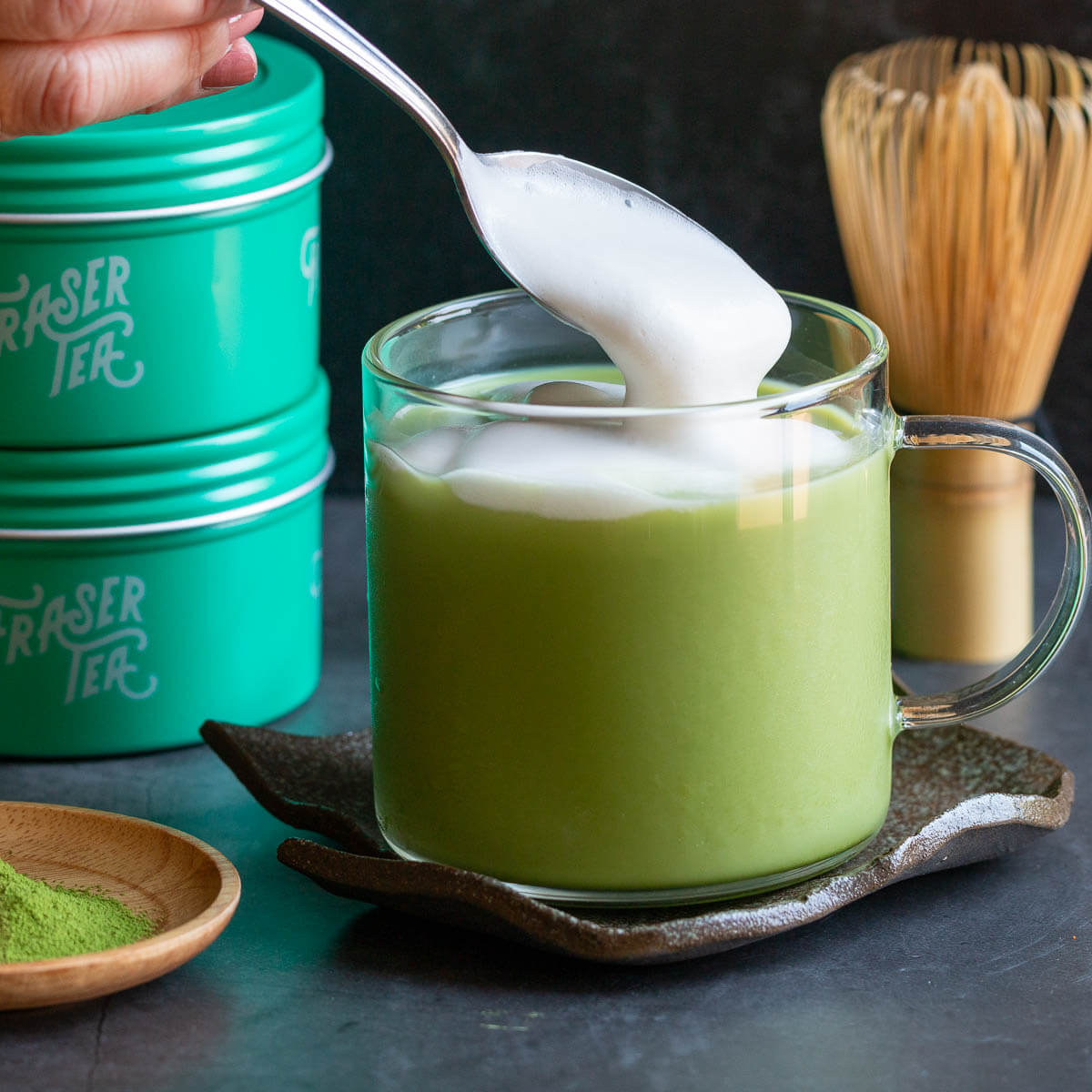 Hot organic matcha is a clear mug with frothy almond milk spooned in on top.