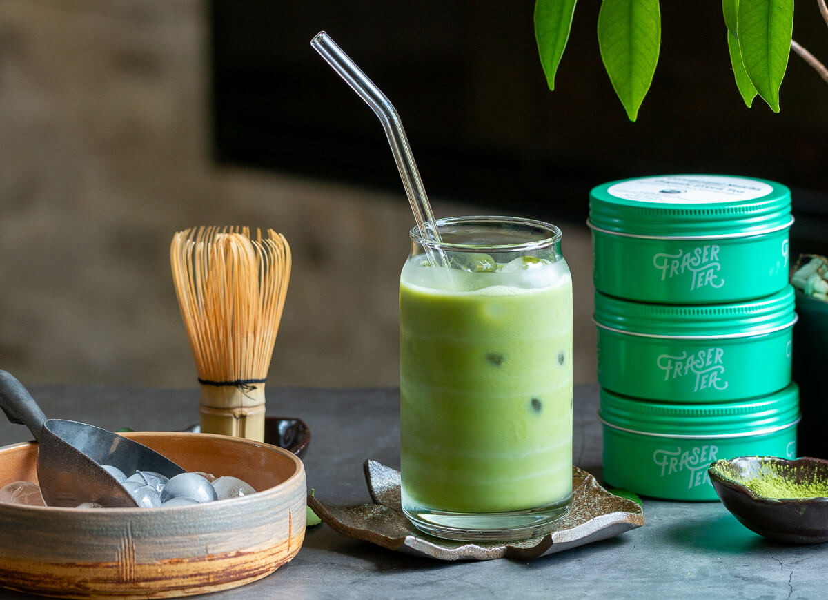 Fraser Tea organic iced matcha latte with whisk, ice and tea canisters.