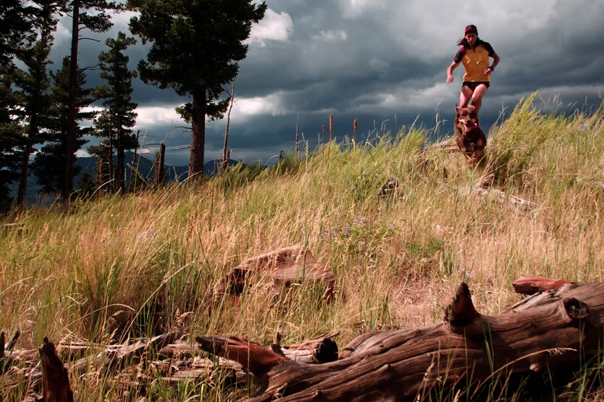 Nicol and Sol trail run along grassy hill on a stormy day.