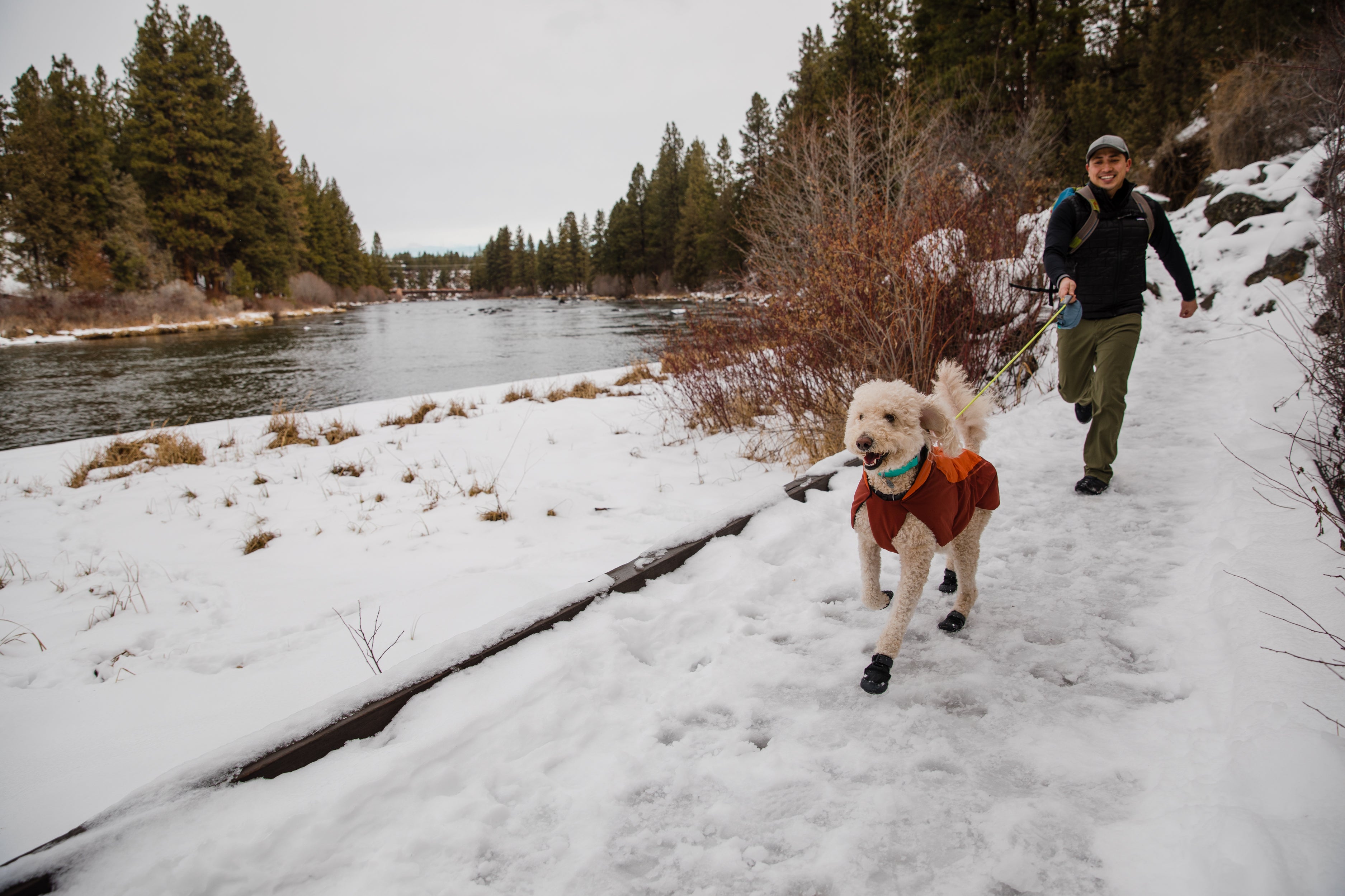 A man runs in the snow with his dog who is wearing Polar Trex™ Dog Boots. 