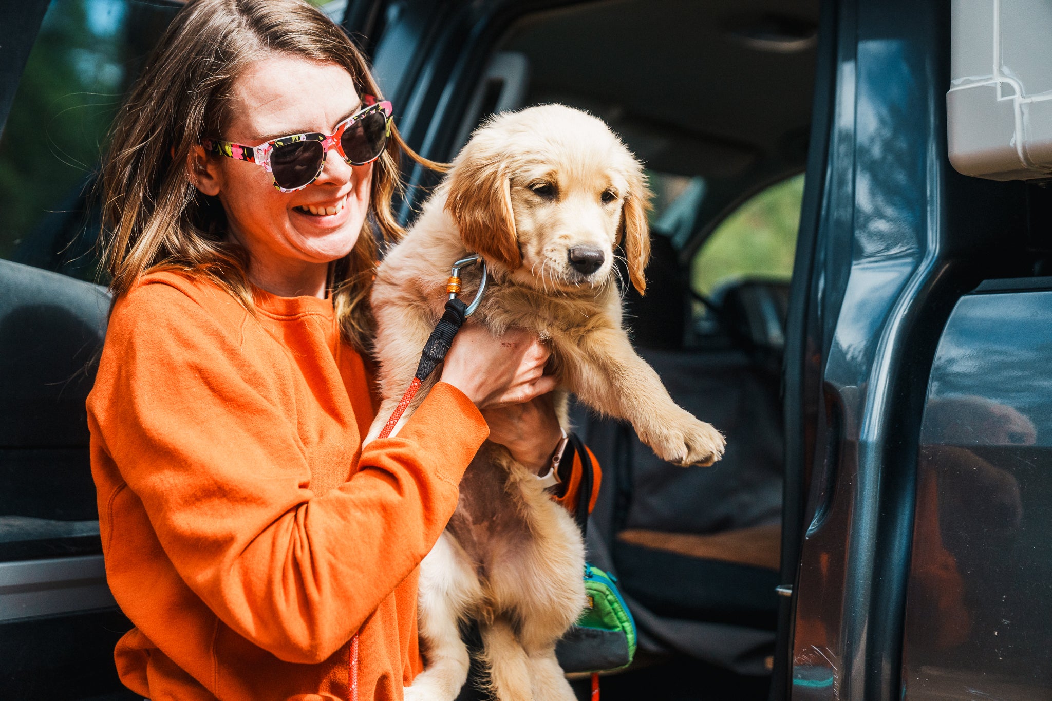 A woman holds her puppy while taking a stretch break on a road trip. 