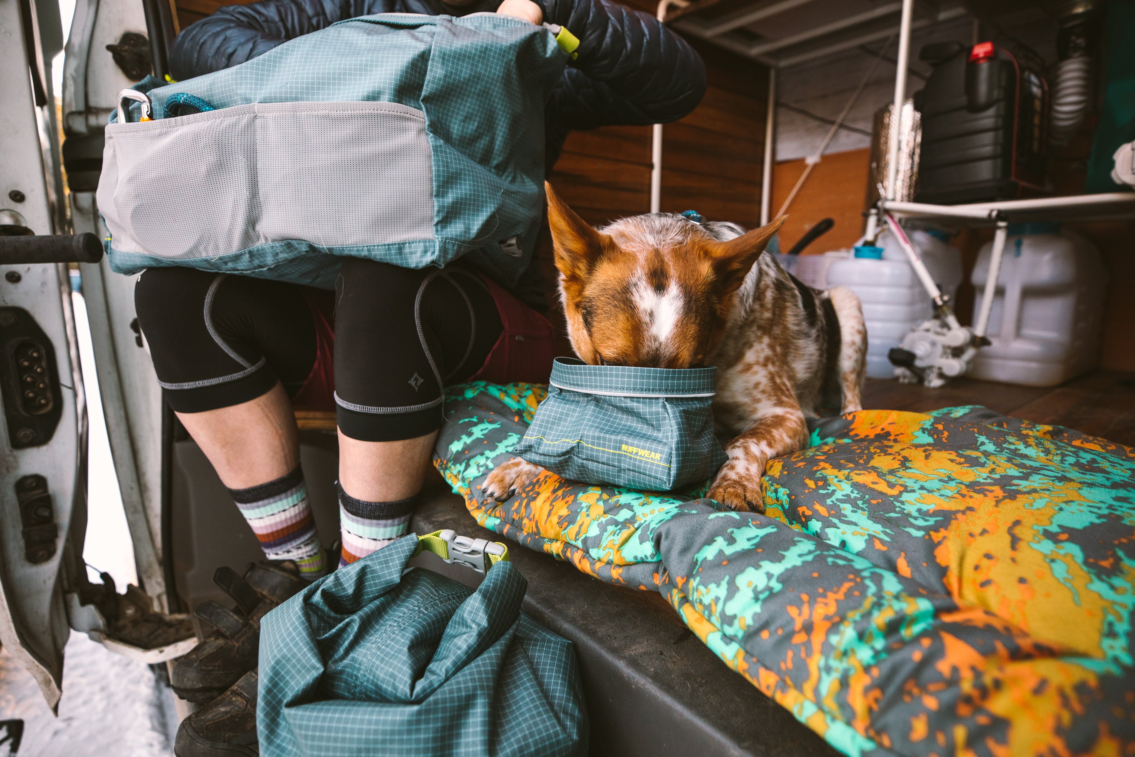 In a camper van, a dog eats from a Ruffwear Great Basin™ Dog Bowl.