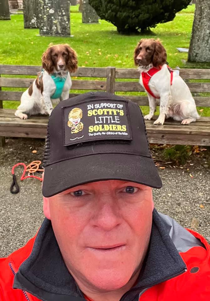 Kerry poses wearing a Scotty's Little Soldiers hat with his two dogs sitting in the background. 