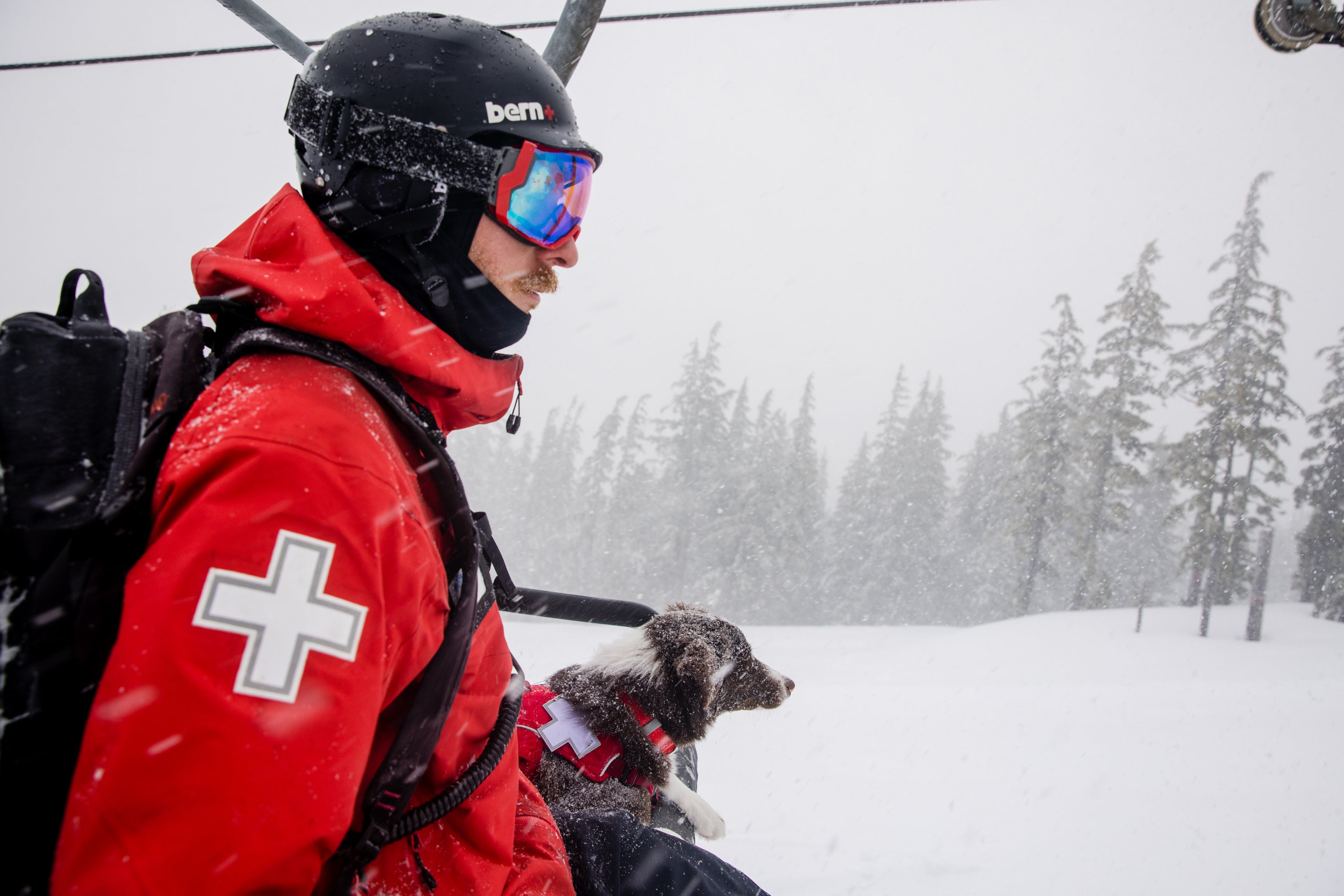 Alex the ski patroller and Ruddy the puppy ride together on the chairlift.