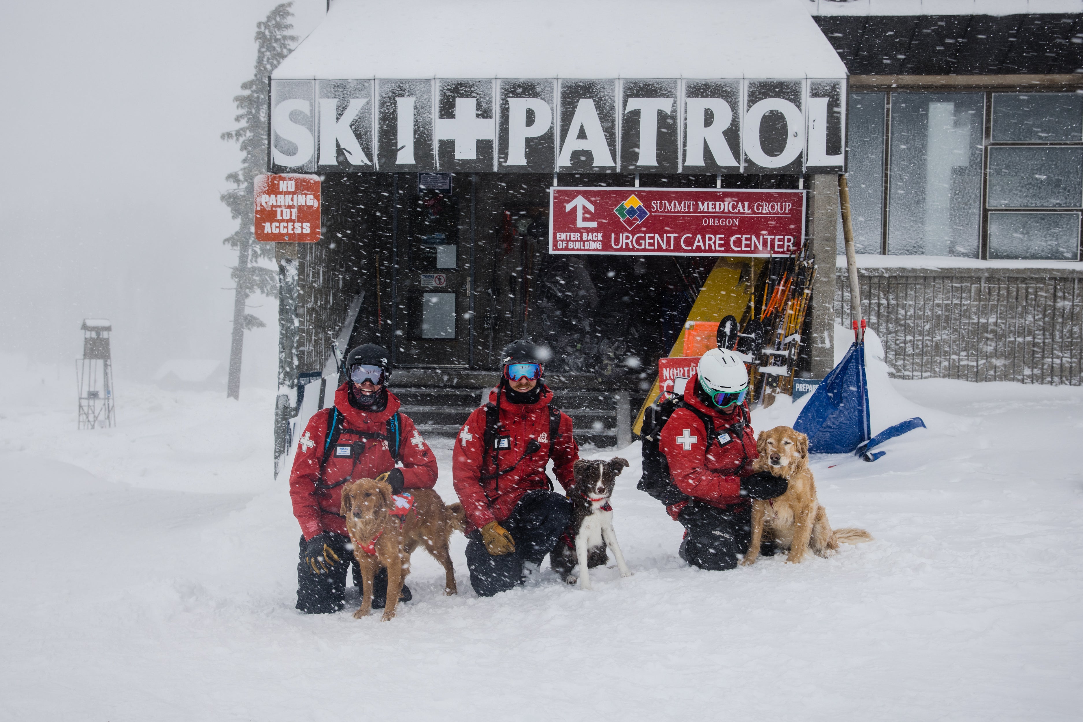 Three ski patrollers pose outside the Ski Patrol Room with their avalanche dogs.