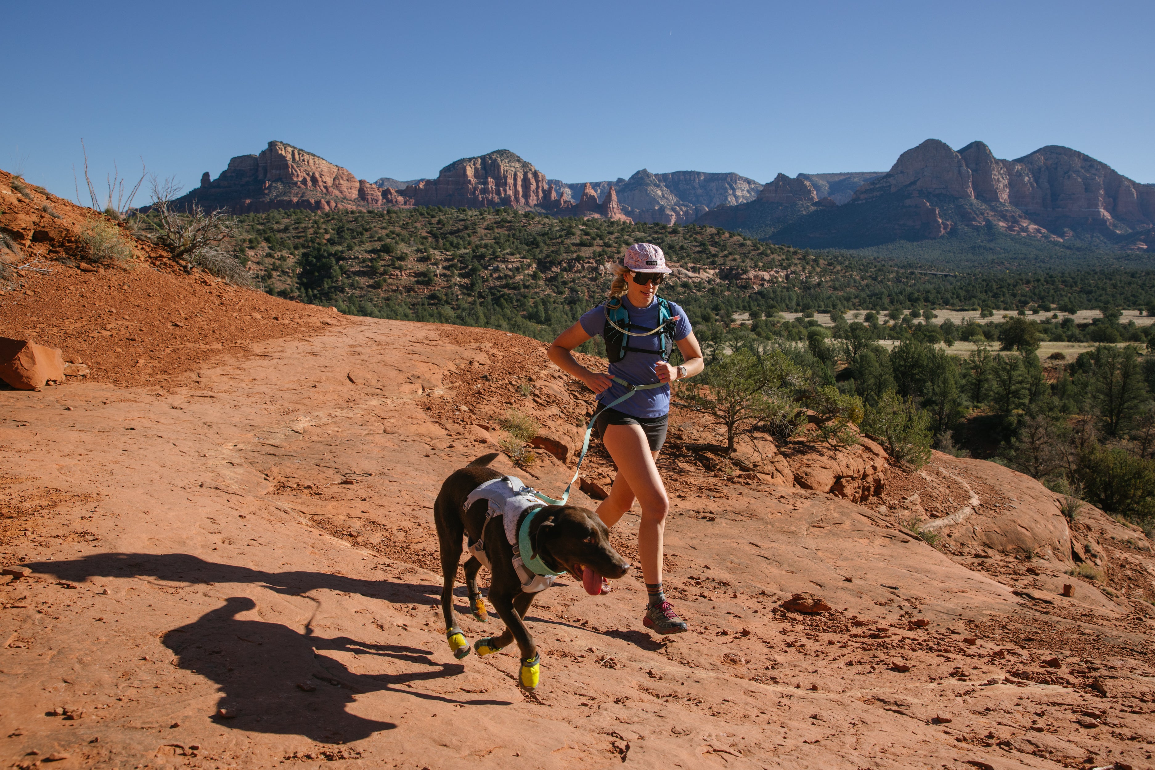 A woman and her dog run on a desert trail.