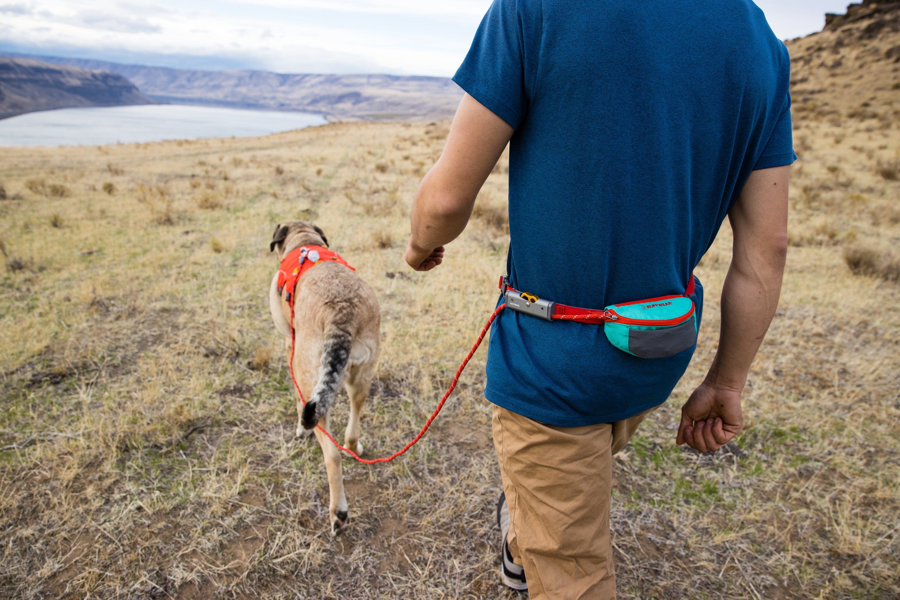 A man hikes with his dog while using Ruffwear's Hitch Hiker leash. 