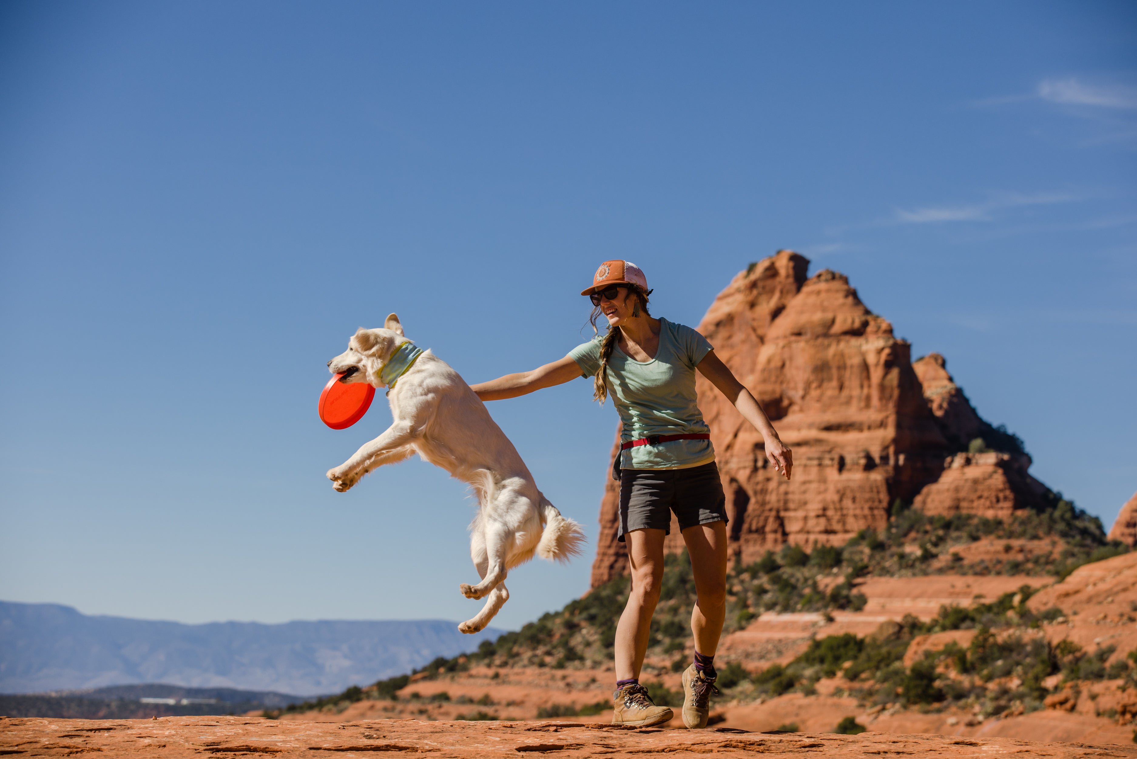 A woman throws the Camp Flyer dog toy for her dog while on a hike. 