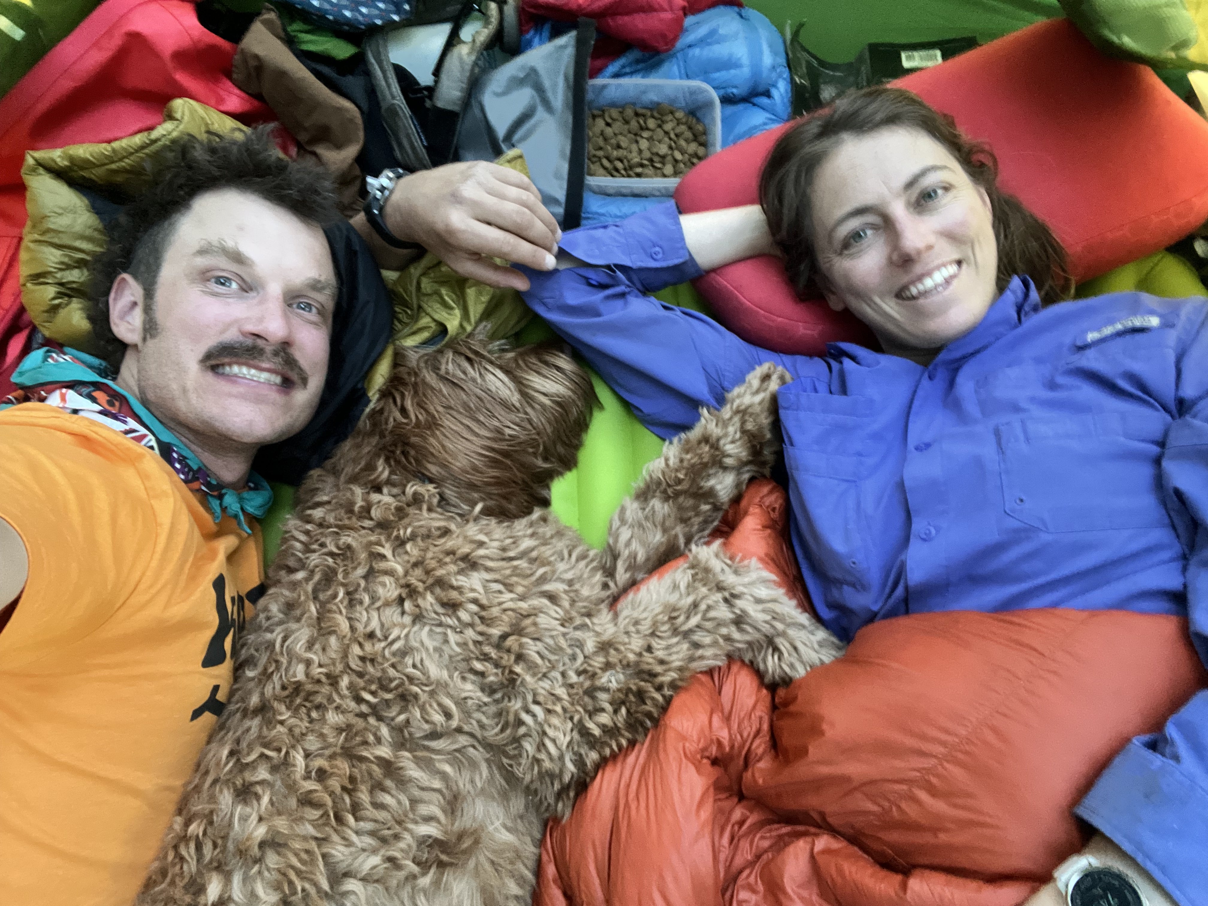 A woman and man rest with their dog on a camping trip. 