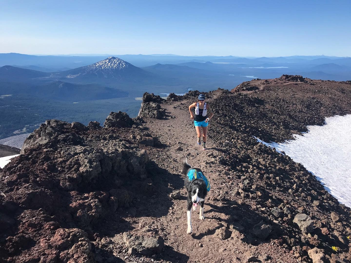 Woman and dog running on trail high up on a rocky mountain summit