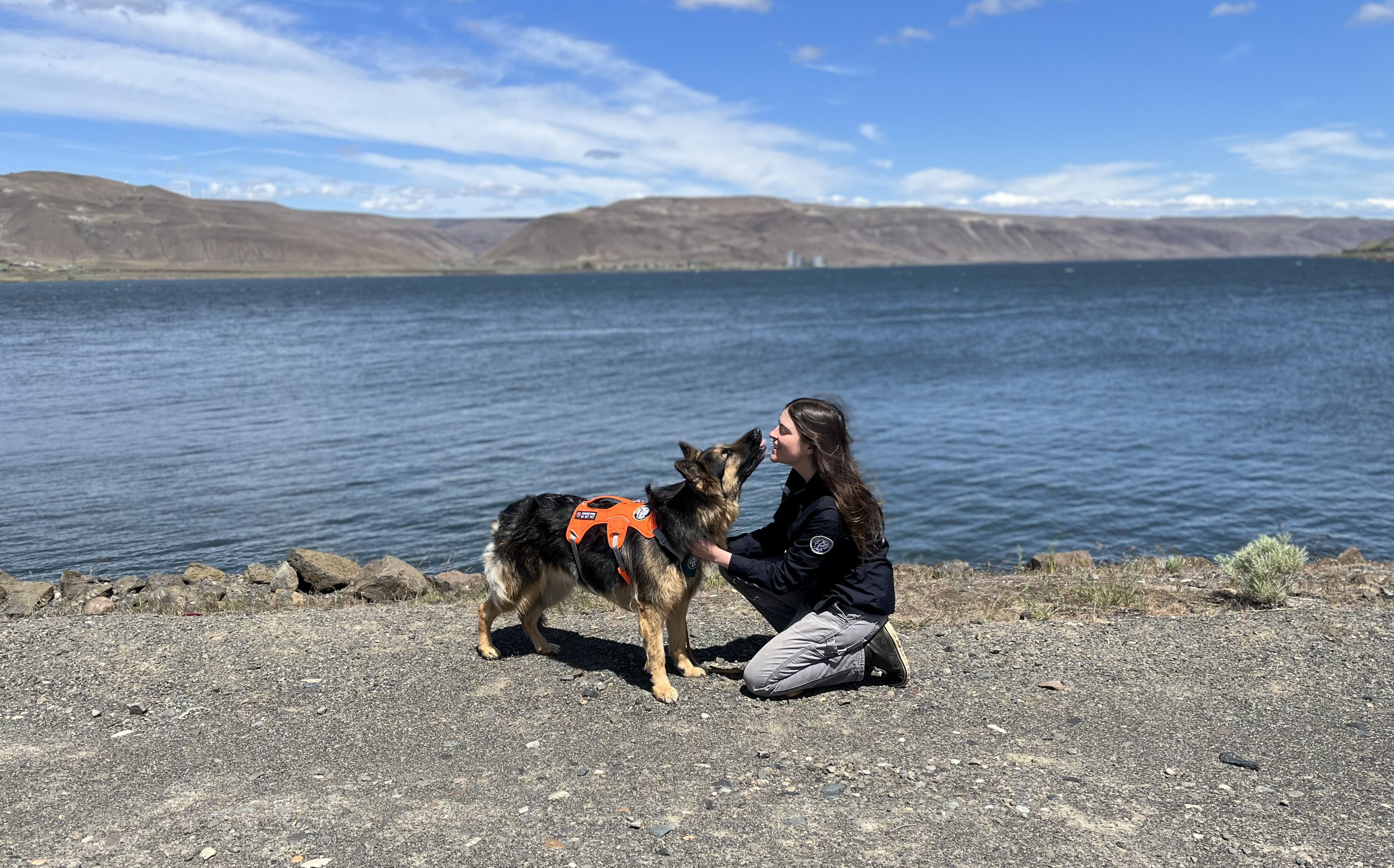 A woman cuddles with her Rogue detection dog, Hugo, by a lake. 