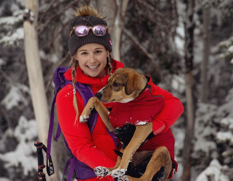 Caroline skiing with dog Lila, who is bundled up in a powder hound jacket.