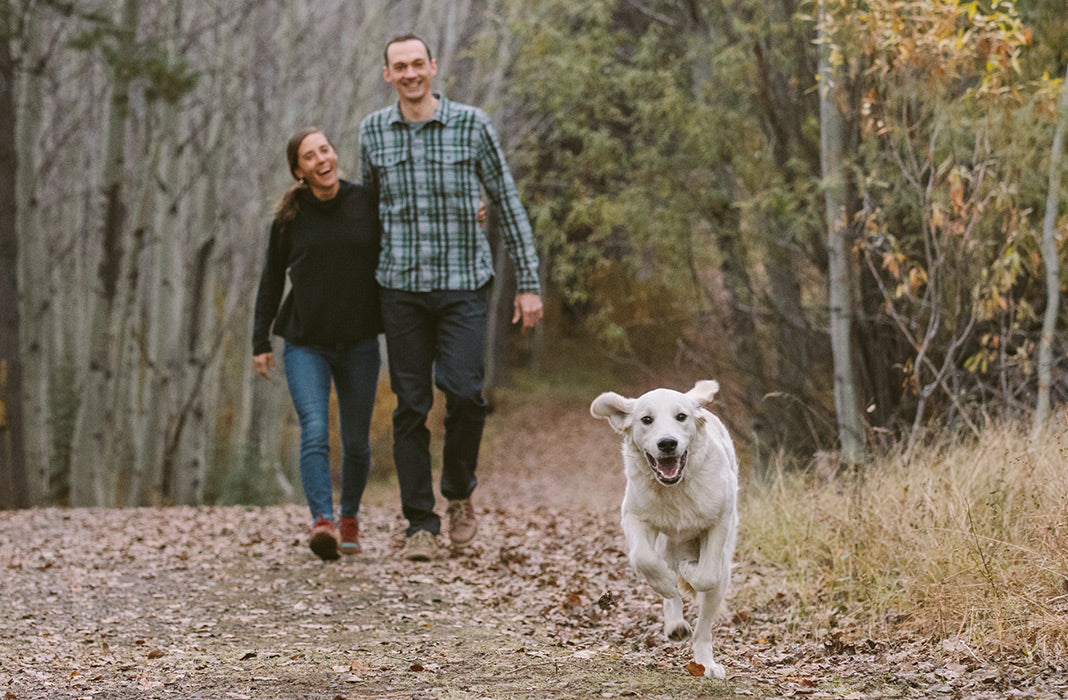 Travis and Carrie walk along trail while pup Atlas runs ahead.