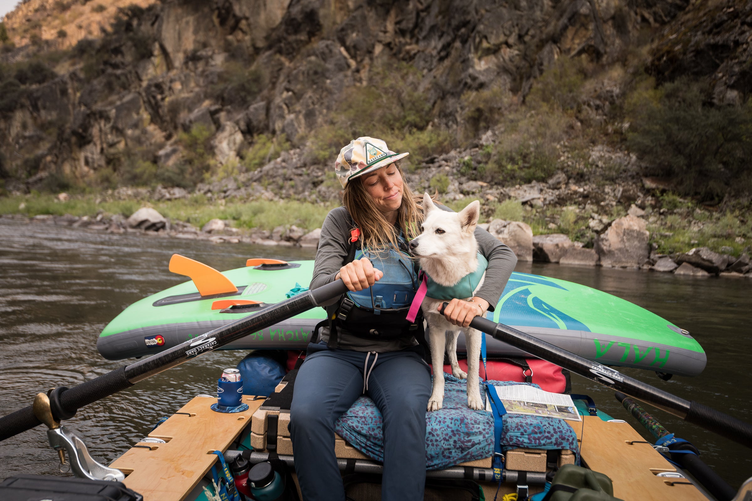 A woman cuddles with her dog while paddling a river raft. 