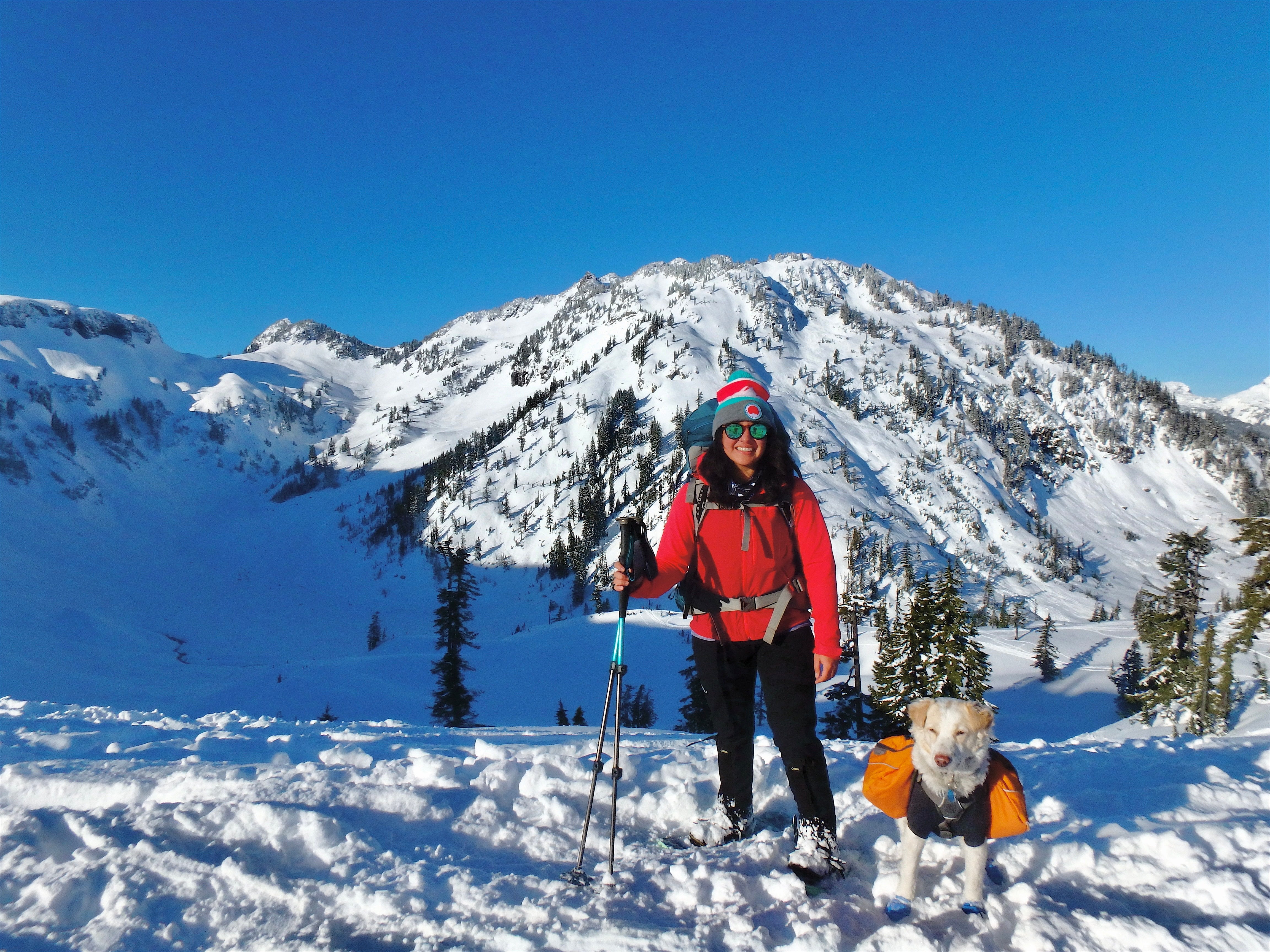 A woman snowshoes in the mountains with her dog by her side. 
