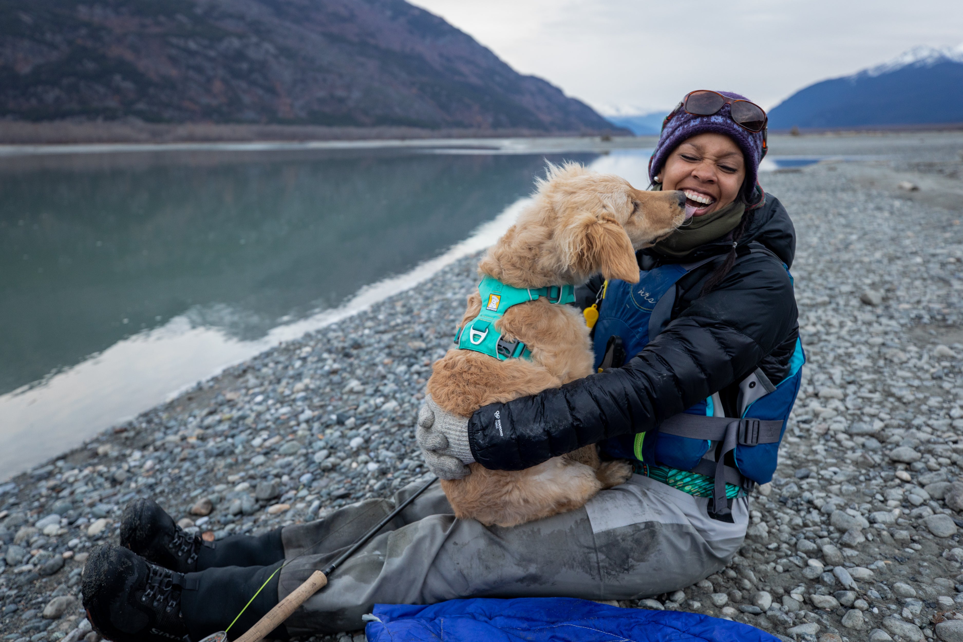 A woman and her dog cuddle and embrace by a lake. 