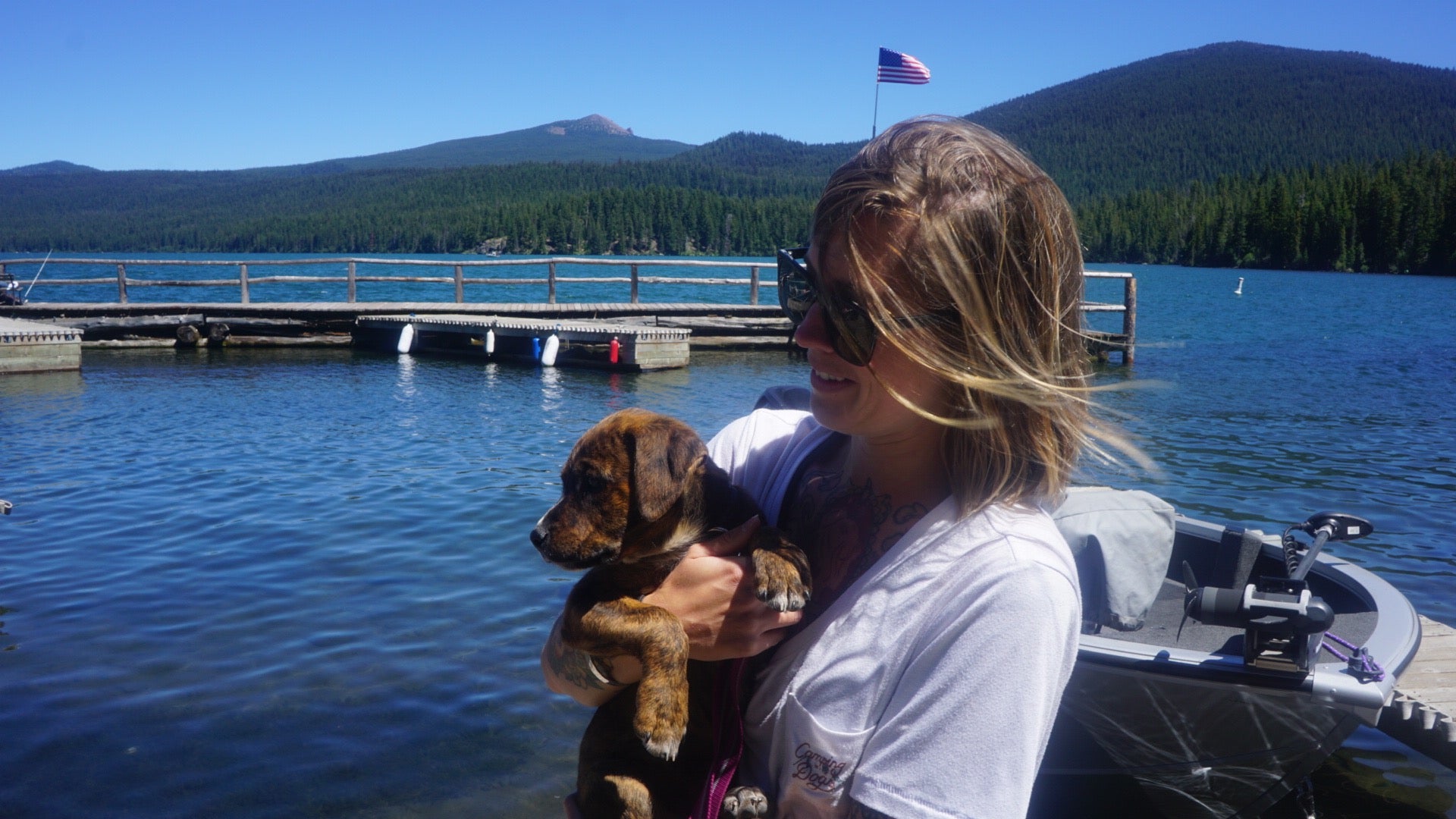 A woman holds her new puppy on a dock by a lake. 