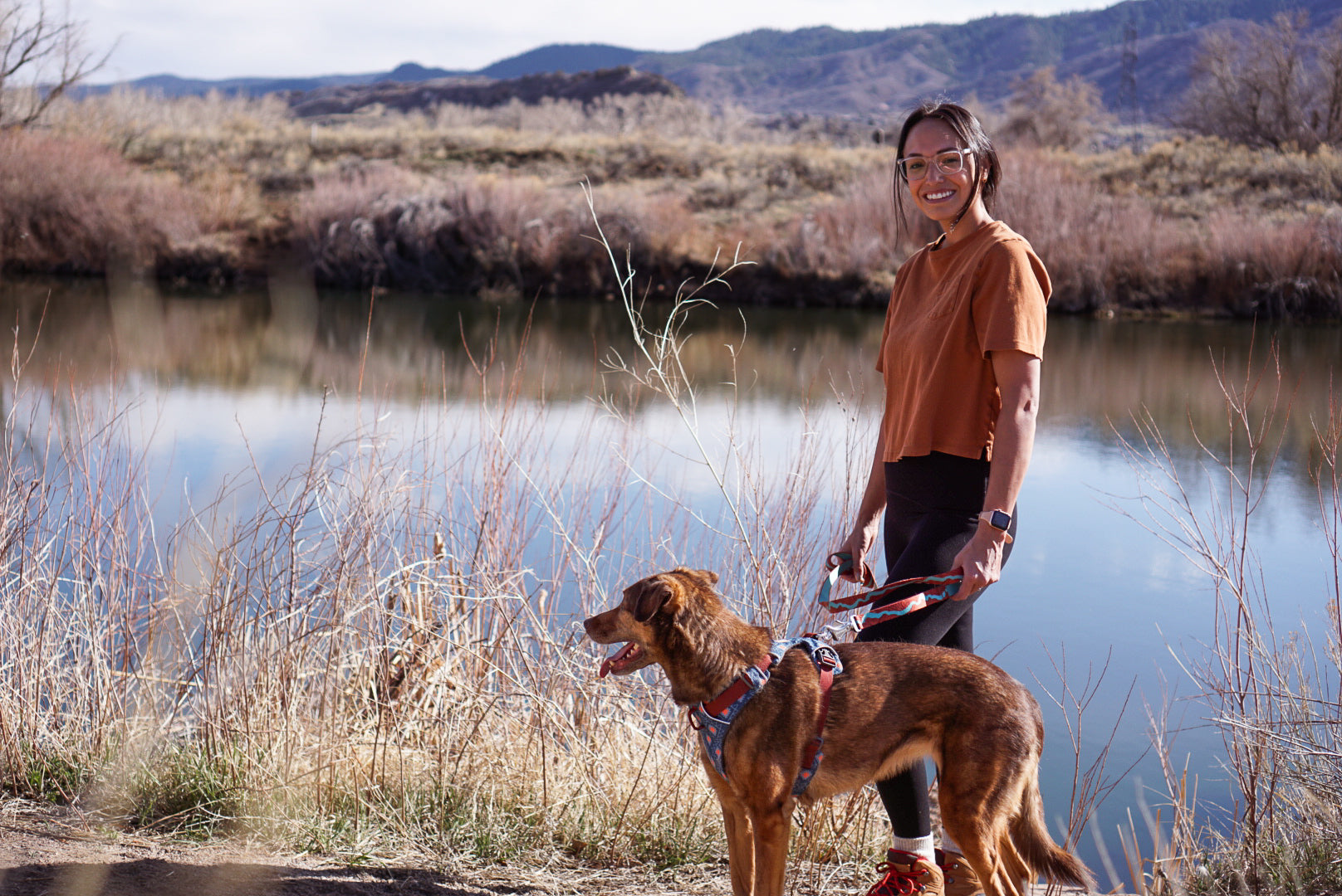 Cali and her dog Mila standing near a pond in a dry landscape.