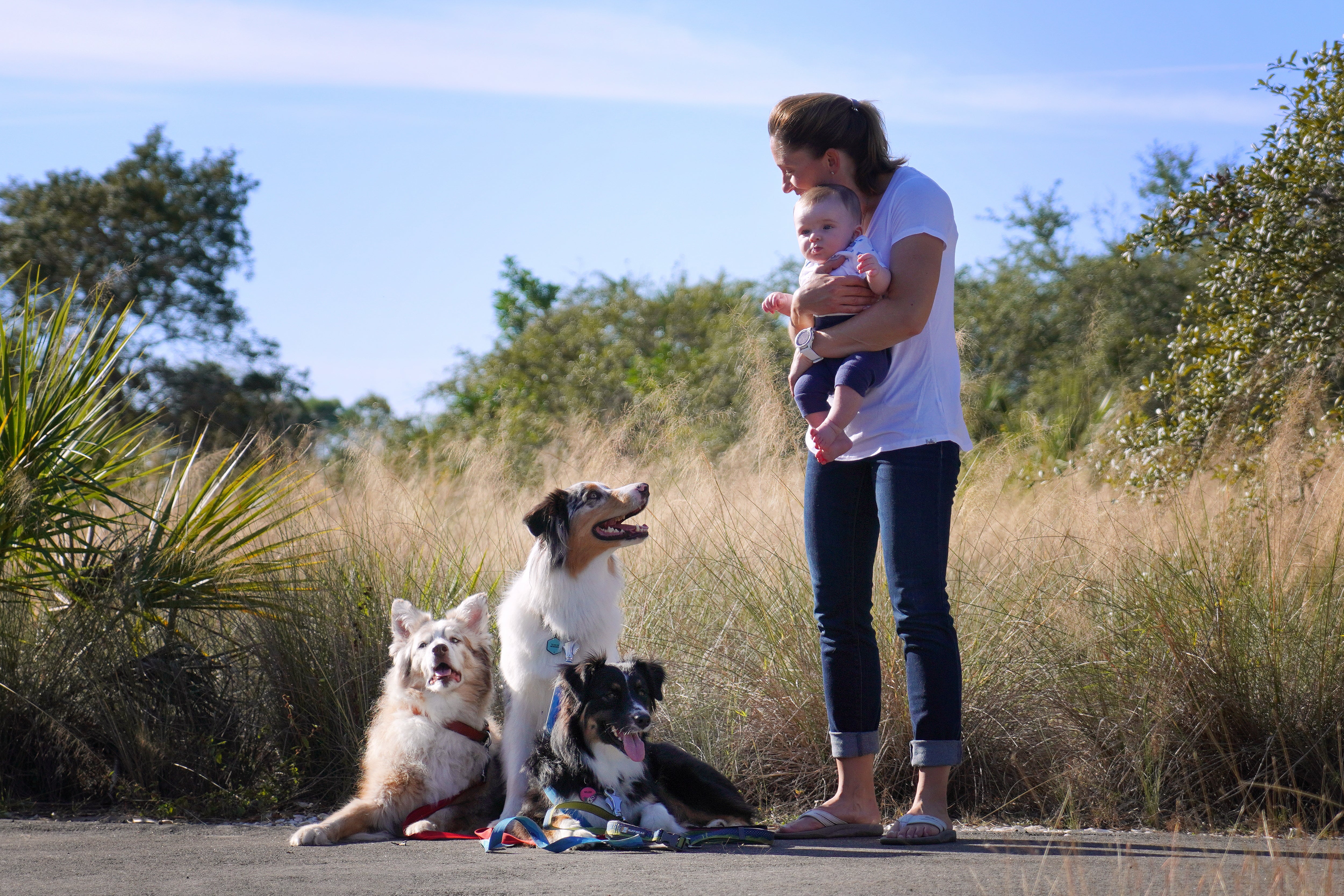 A woman holds her baby and smiles at her three dogs. 