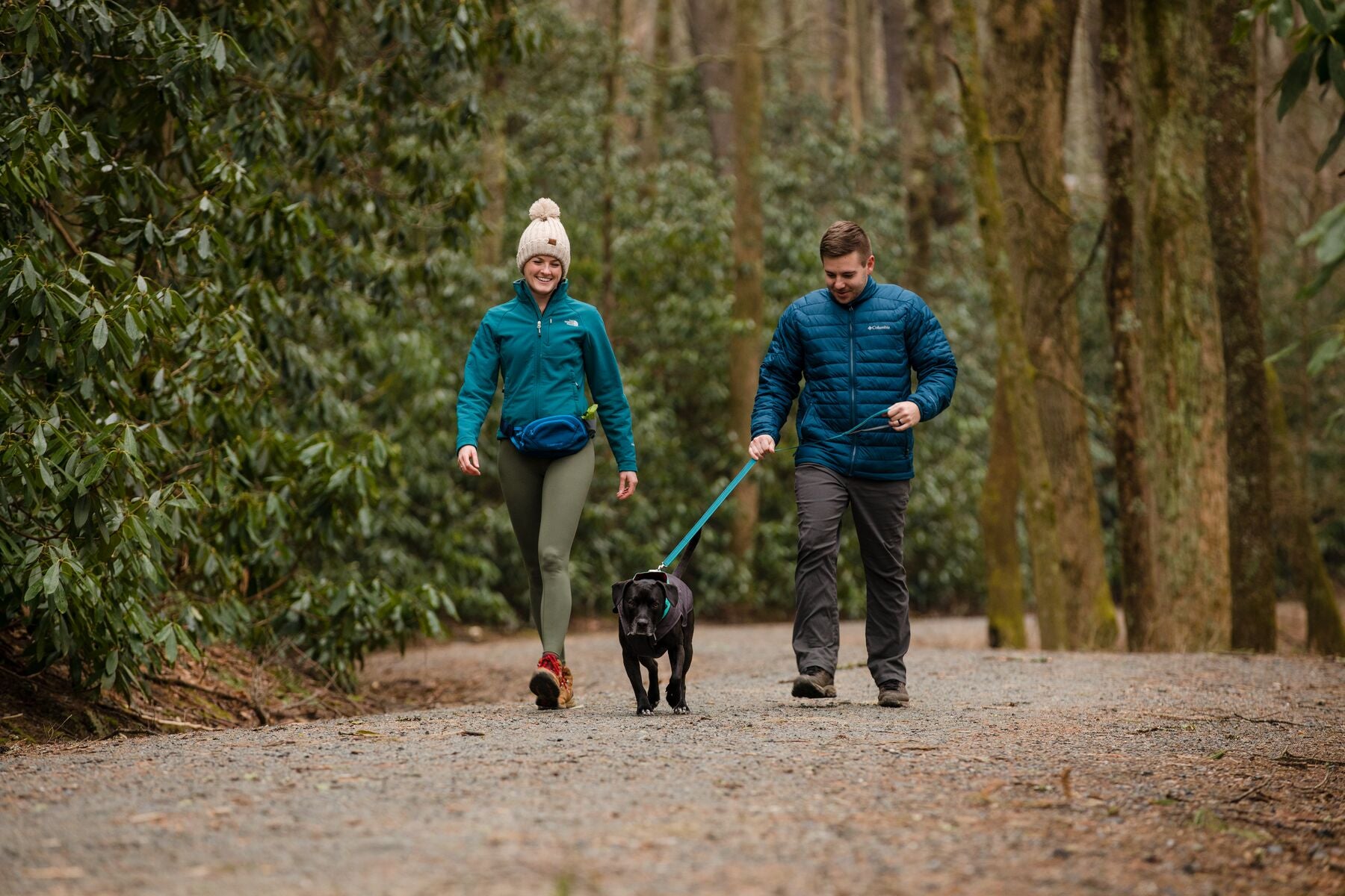 Woman wearing home trail hip pack walks with man and dog in a park.