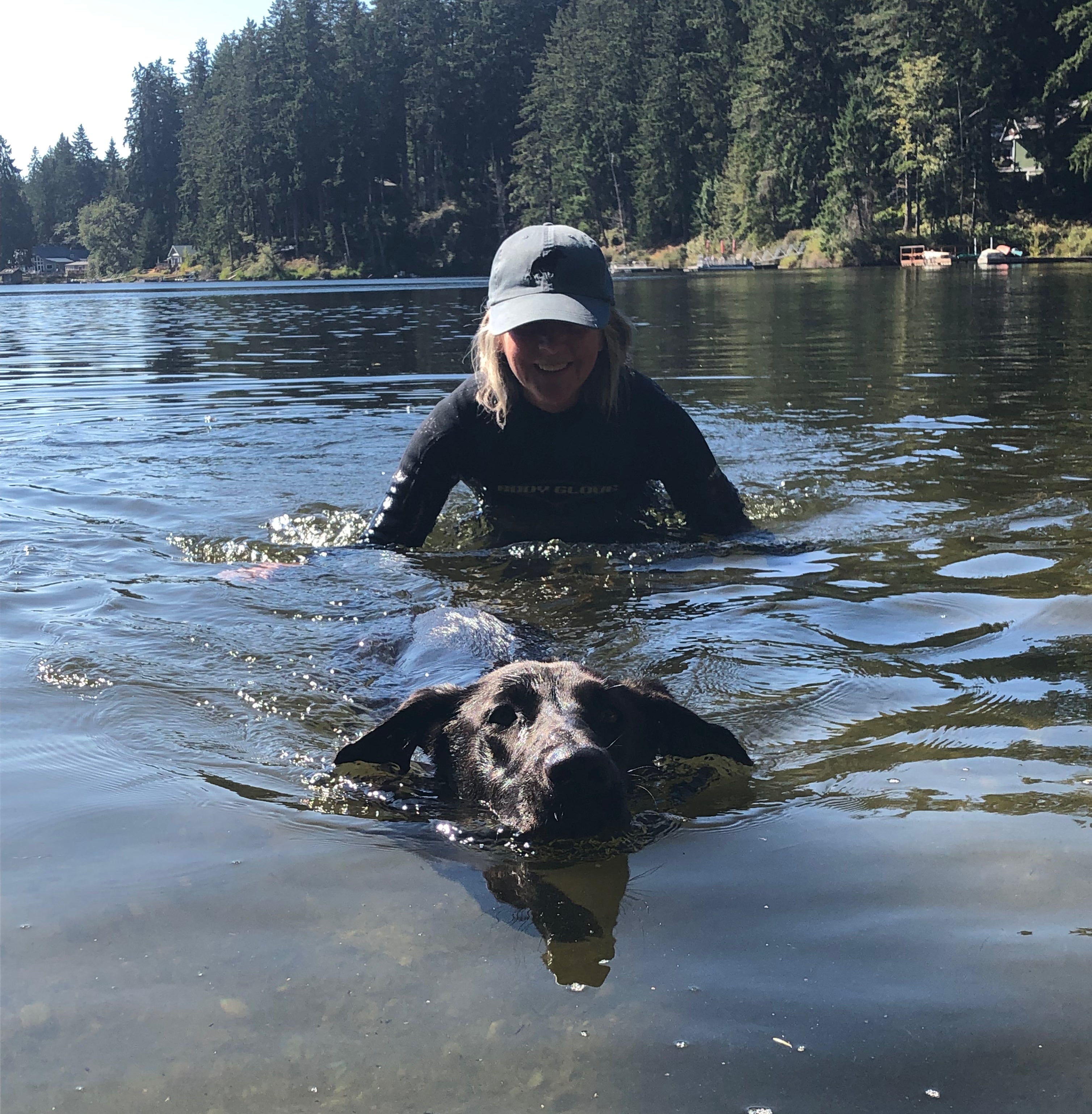 A woman and her dog swim together in a lake. 