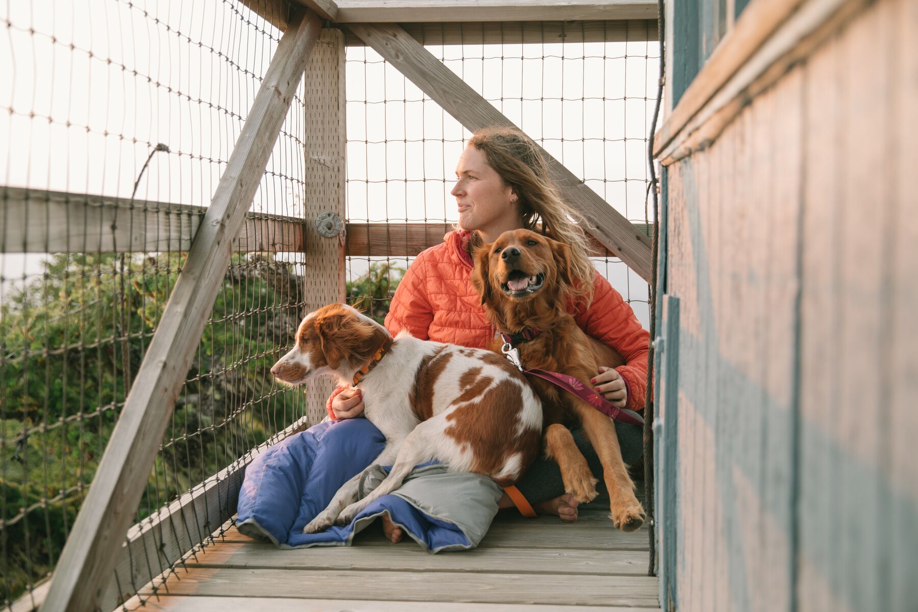 Elise enjoys the view from a fire lookout with dogs Ubu and Bailey wrapped in a clear lake blanket at her side.