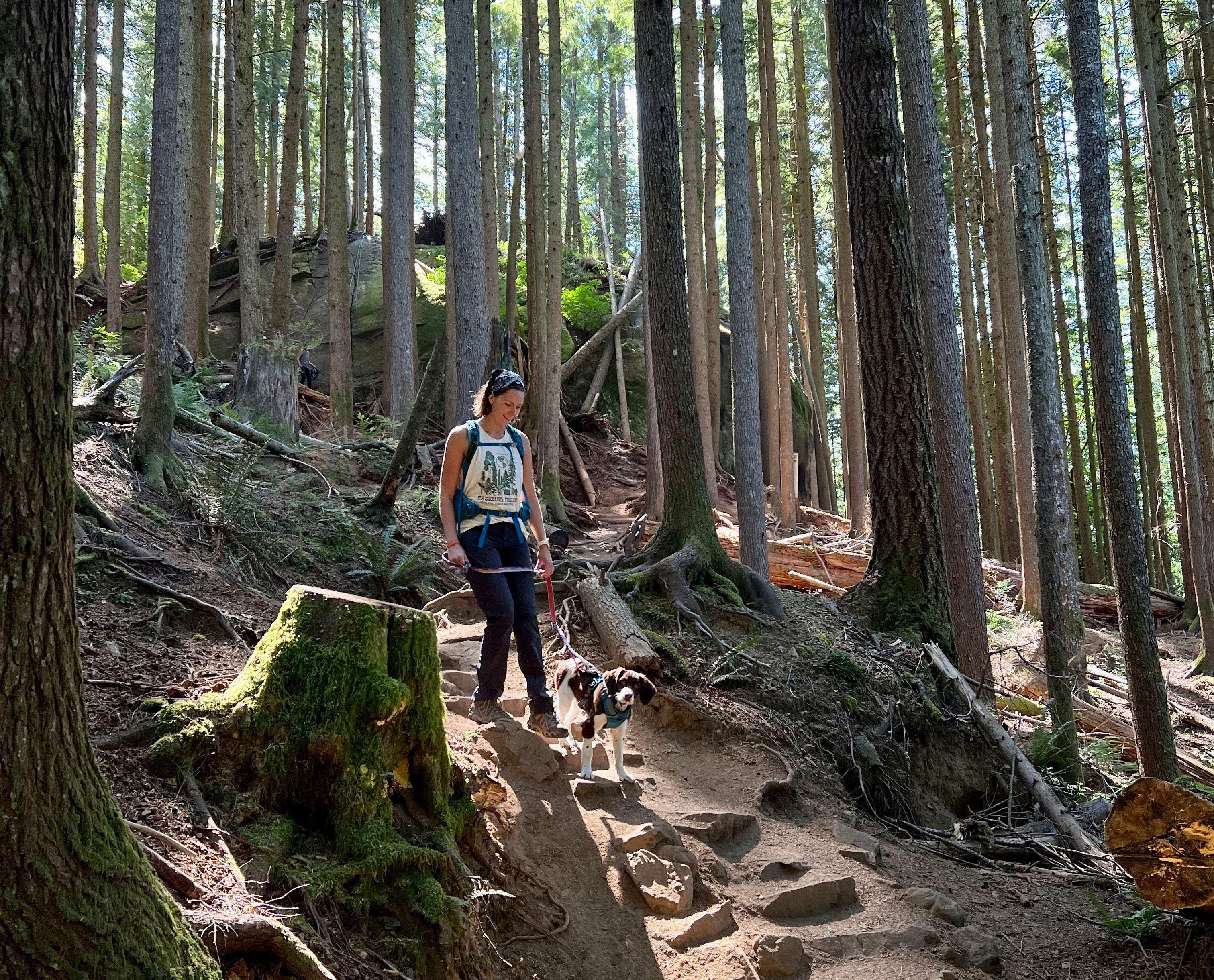 A woman hikes with her puppy in the woods. 