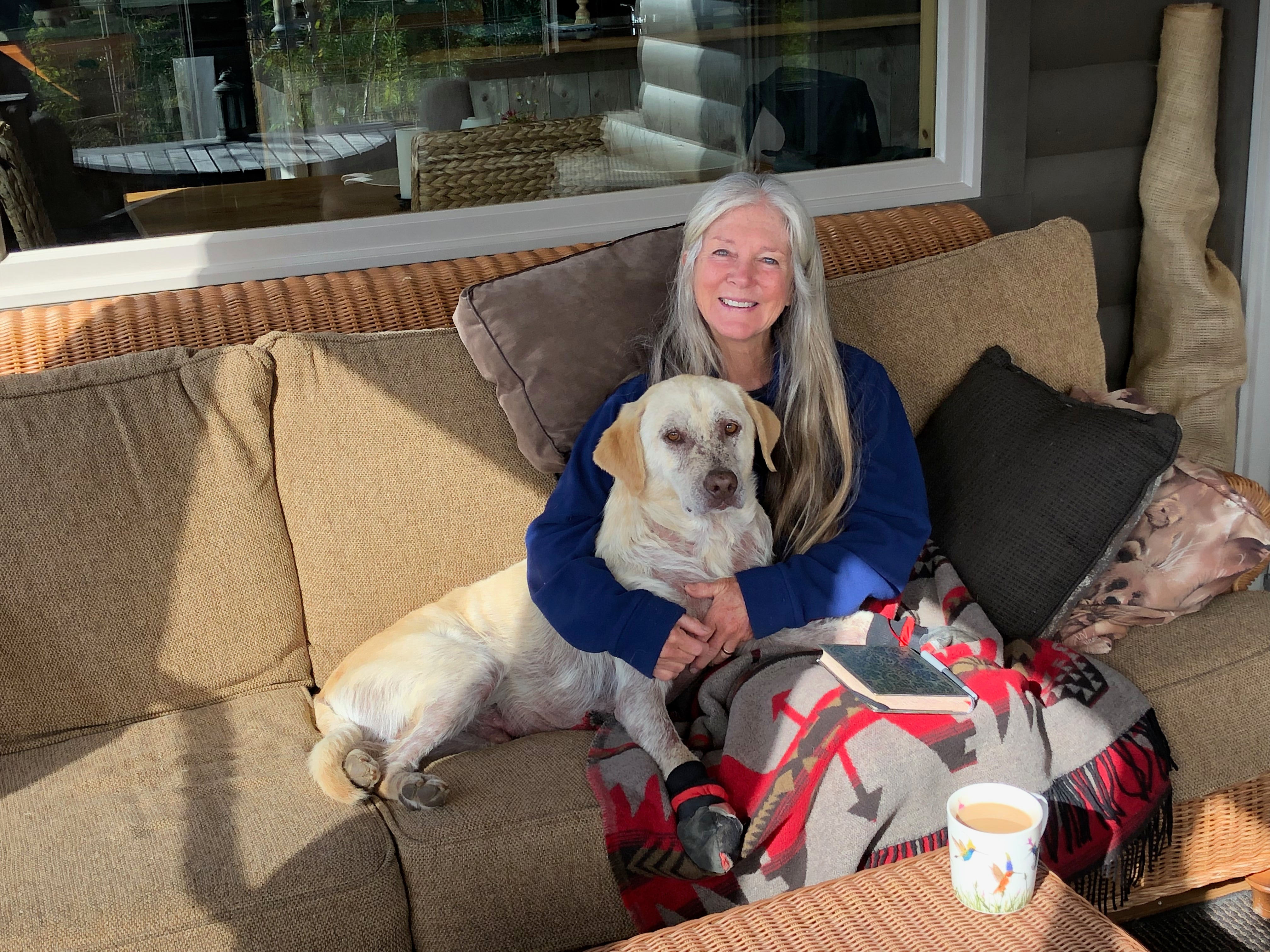 A woman and her yellow lab dog cuddle on the couch. 