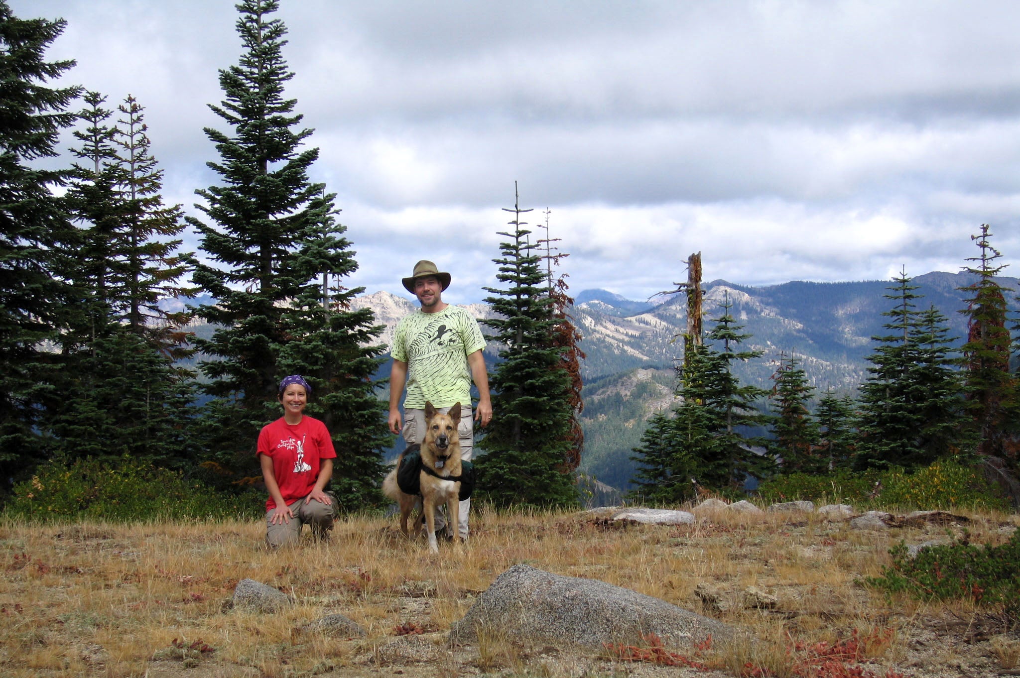 Rene and Jim stand with dog Jerry wearing dog backpack.