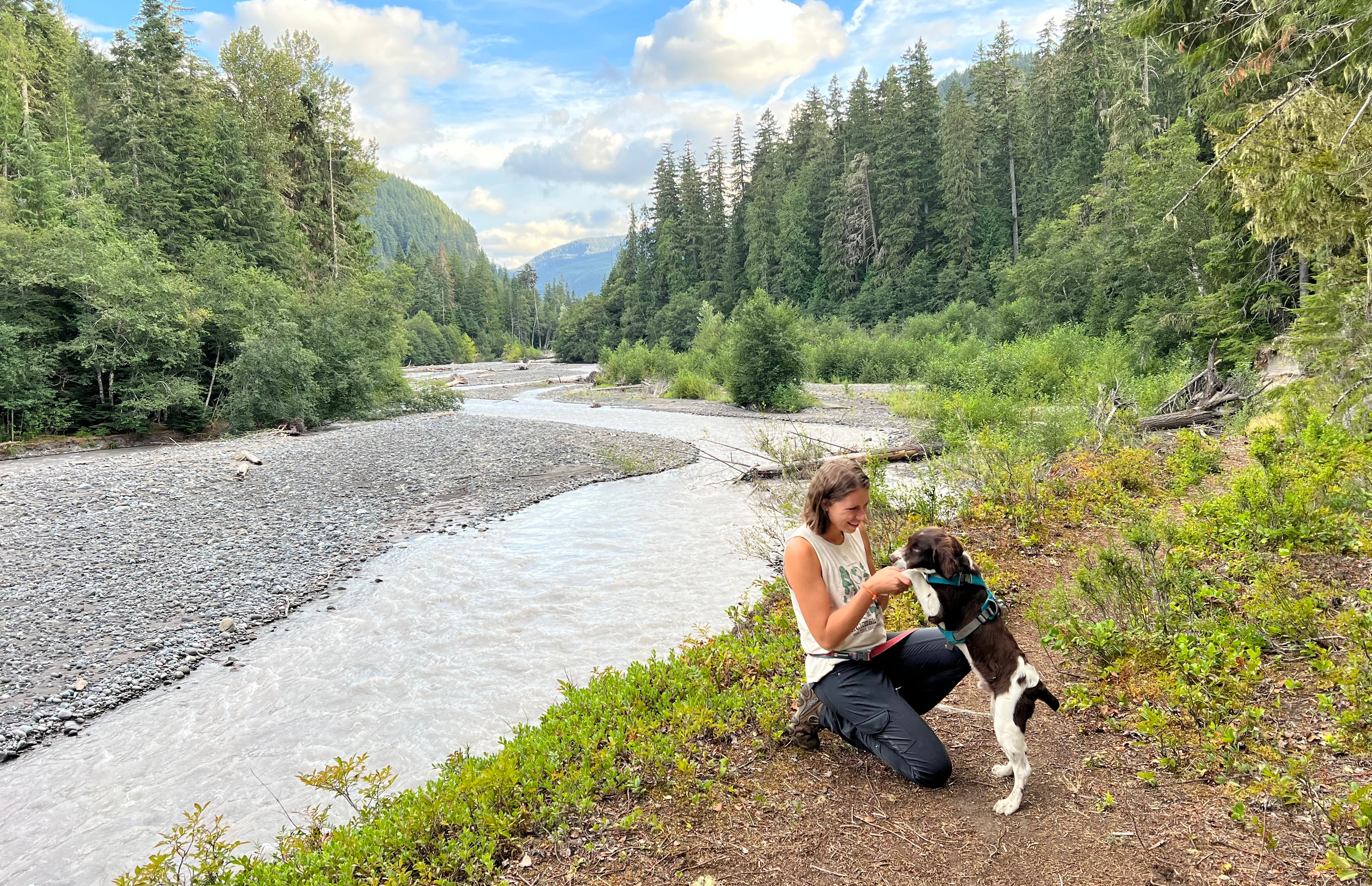 A woman cuddles with her puppy while they sit by a lake. 