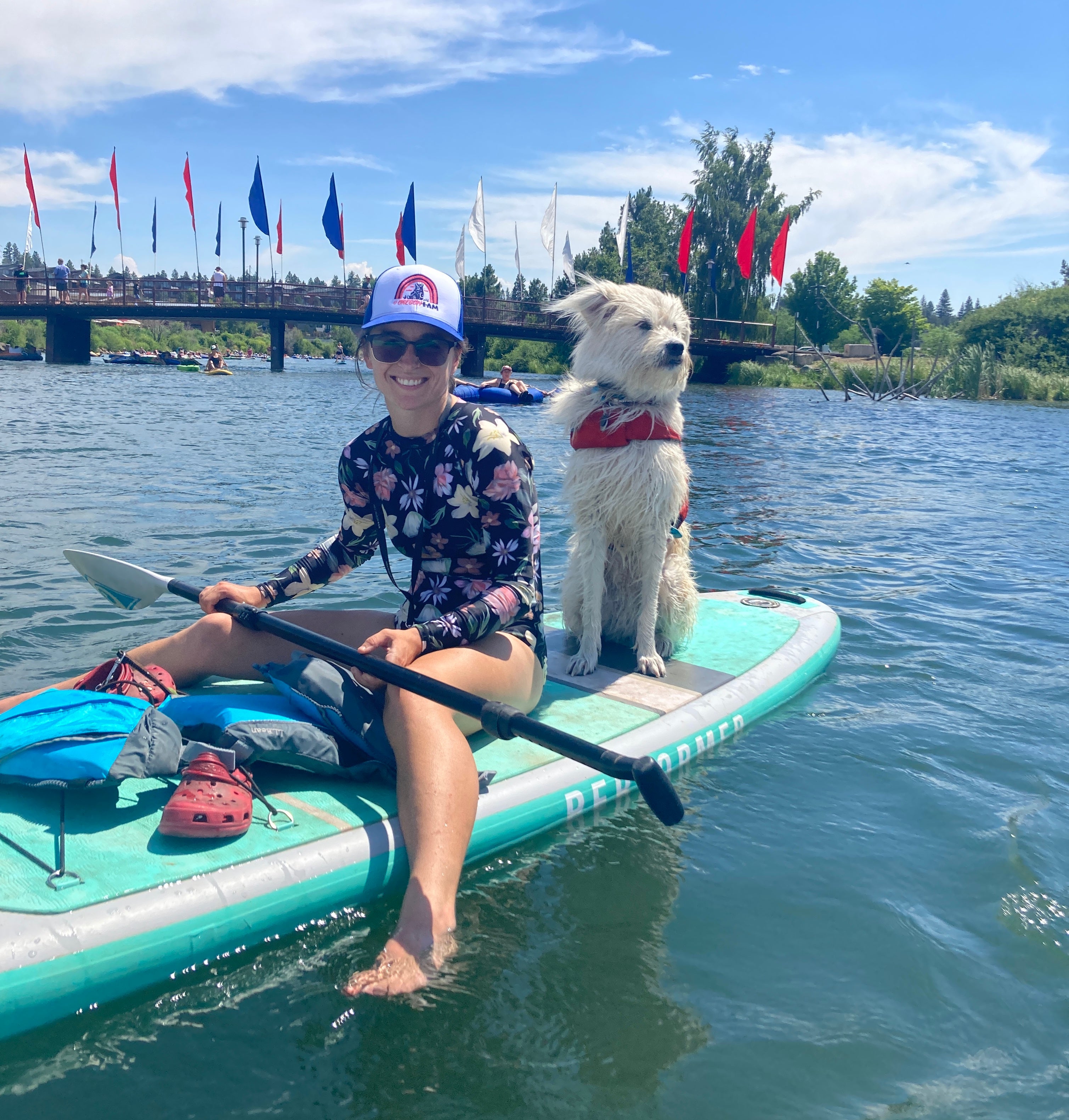 A woman sits on a stand up paddleboard with her dog. 