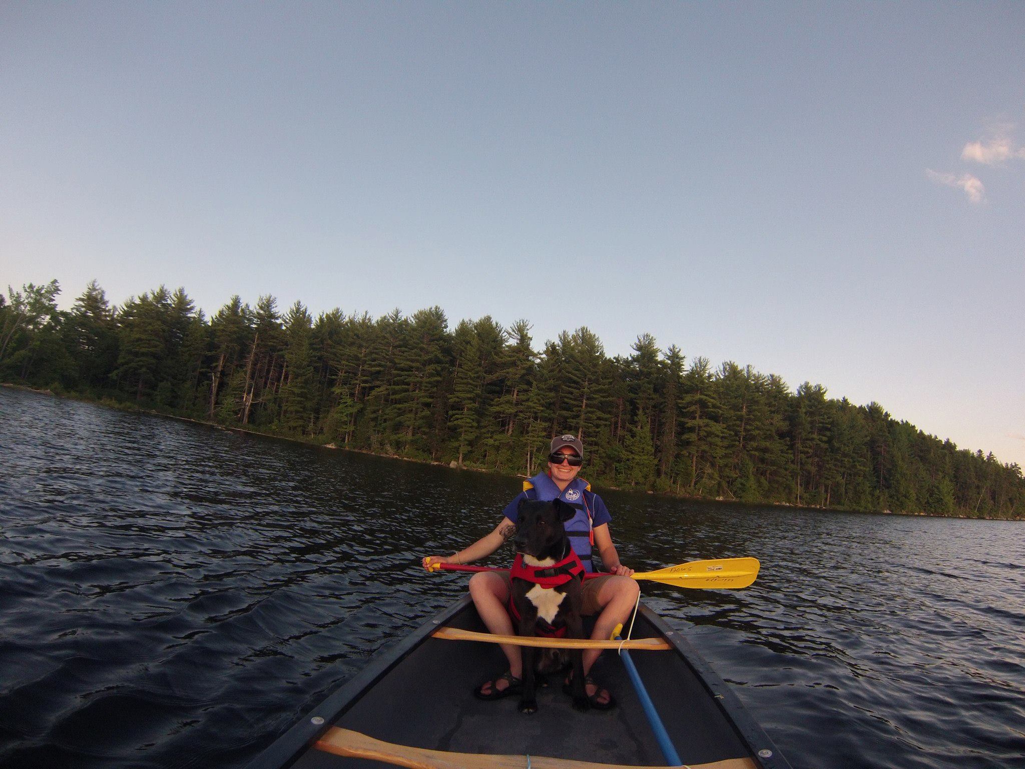 A woman and her dog sit in a canoe on a lake. 