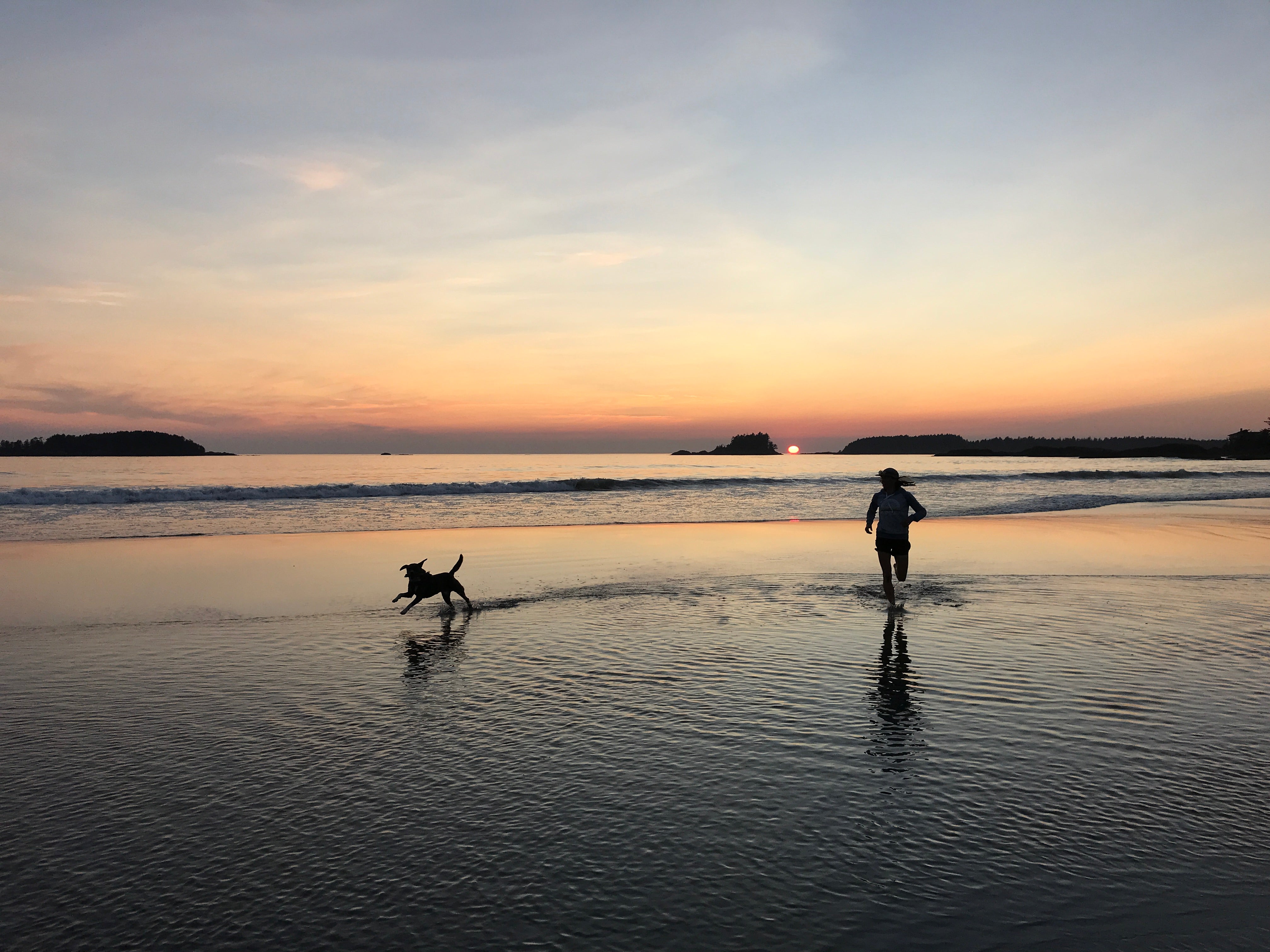 human and dog running on beach at sunset